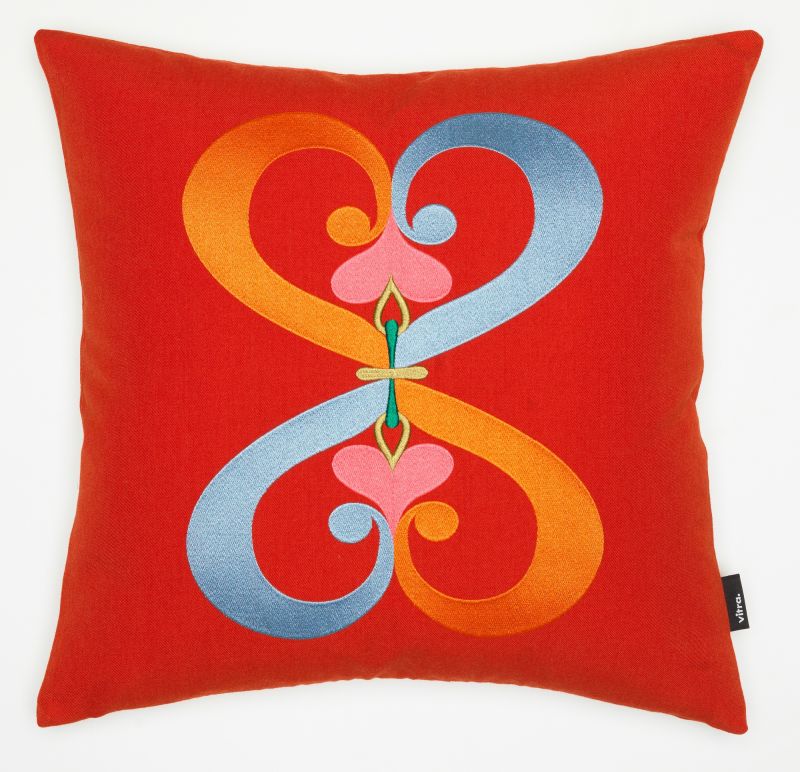 Vitra Kissen mit rotem Bezug und gesticktem, abstraktem Doppelherz-Motiv in Orange und Blau.